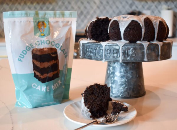 Glazed gluten-free chocolate cake displayed next to Be Free Cafe's Chocolate Cake Mix.